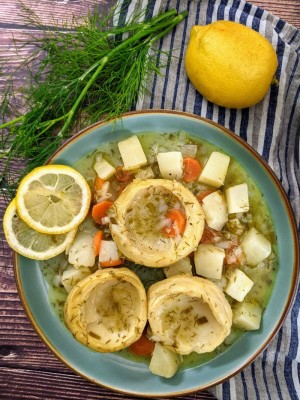 Artichokes stew served on blue plate with lemon slices on the side and a bunch of dill next to the plate.