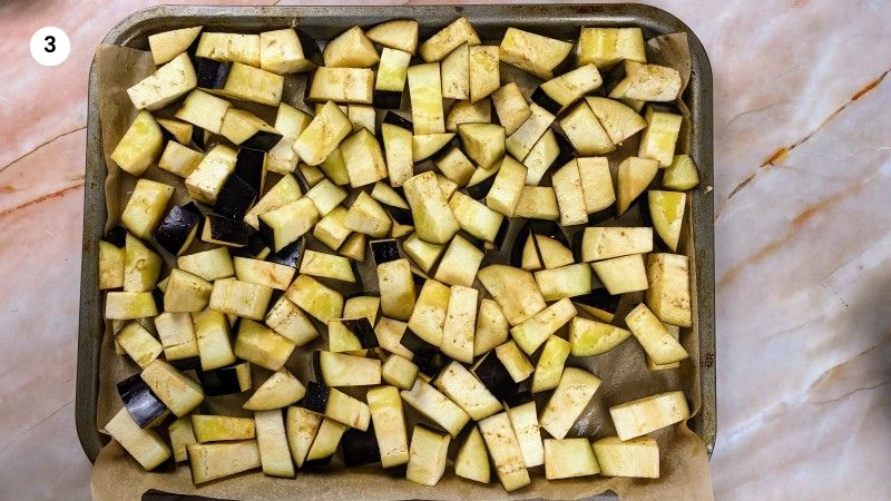 Adding the eggplant cubes to a lined tray to roast.