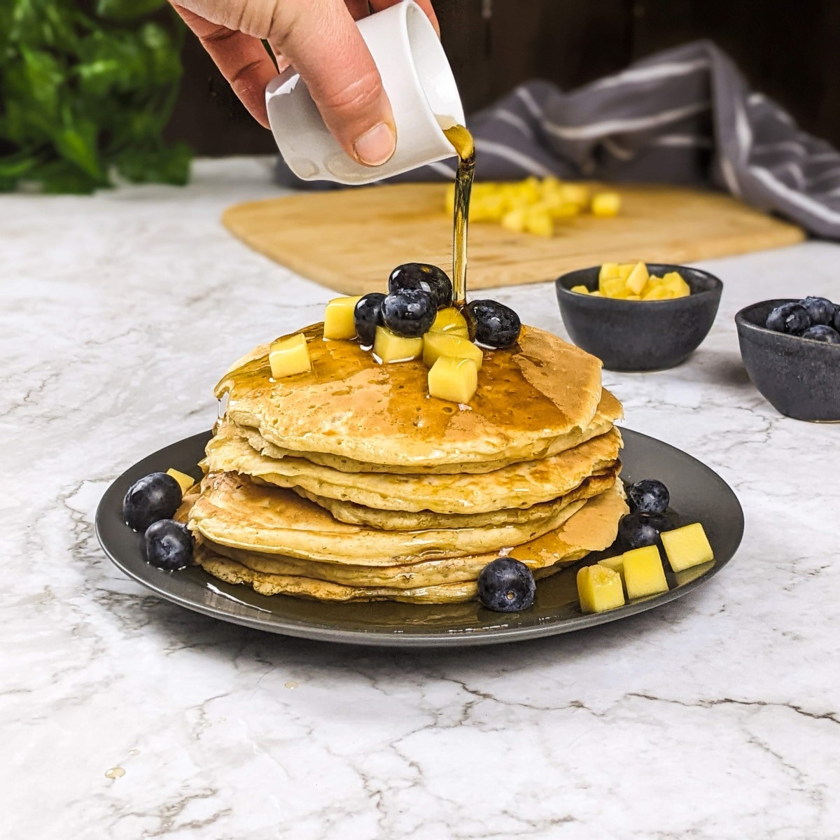 A stack of pancakes with mango and blueberries on top and running maple.