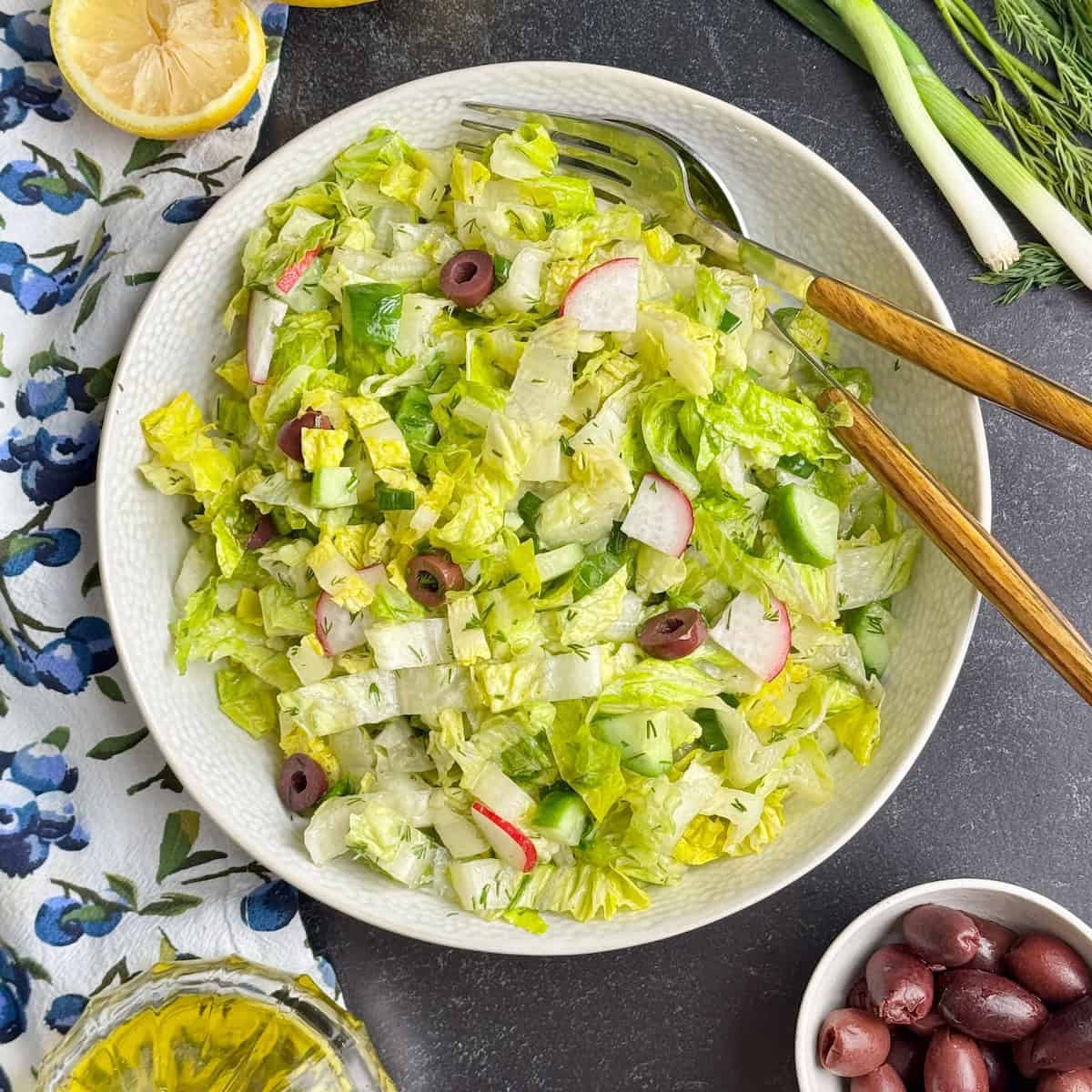 Greek lettuce salad served in a bowl next to halved lemon, fresh dill and olives.