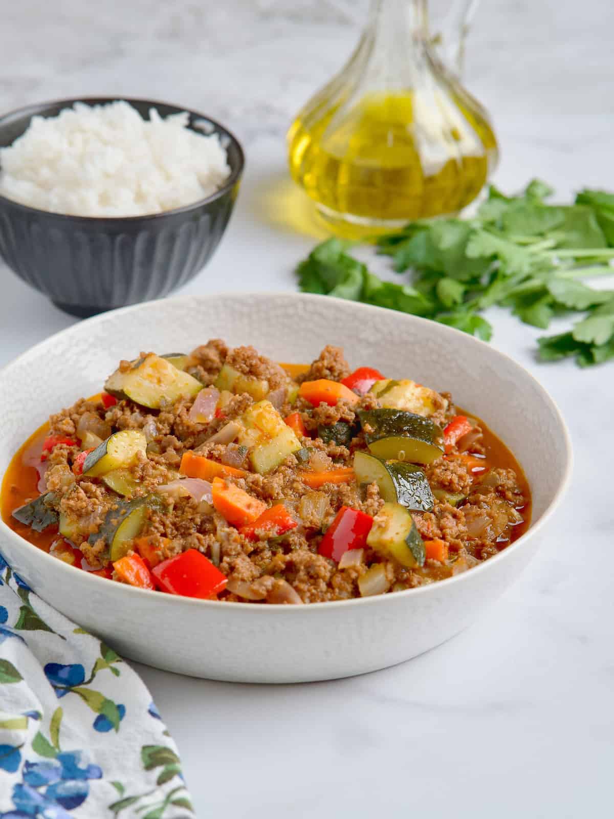 Ground beef with vegetables served on a white bowl next to olive oil, rice and fresh parsley Ground beef with vegetables served on a white bowl next to olive oil, rice and fresh parsley.