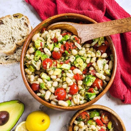 Cannellini beans salad served in a wooden bowl next to a lemon and avocado.