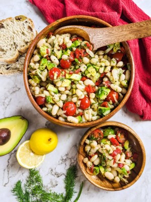 Cannellini beans salad served in a wooden bowl next to a lemon and avocado.