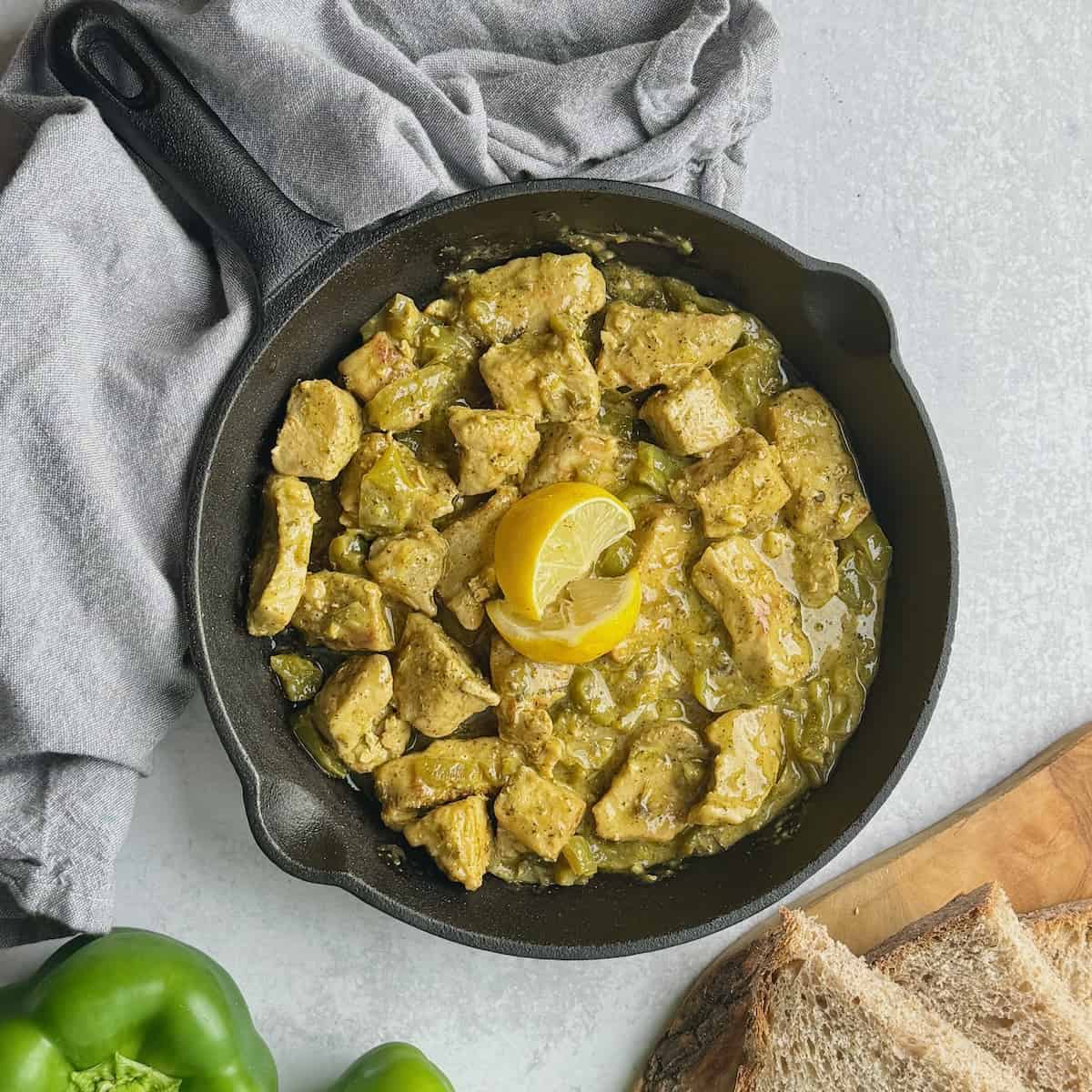 Pan fried pork chunks in a frying pan next to slices of bread and green bell pepper.