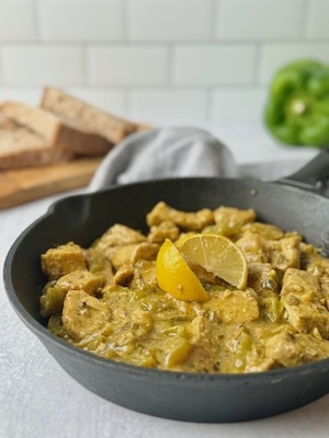 Pan fried pork chunks in a frying pan next to slices of bread and green bell pepper.