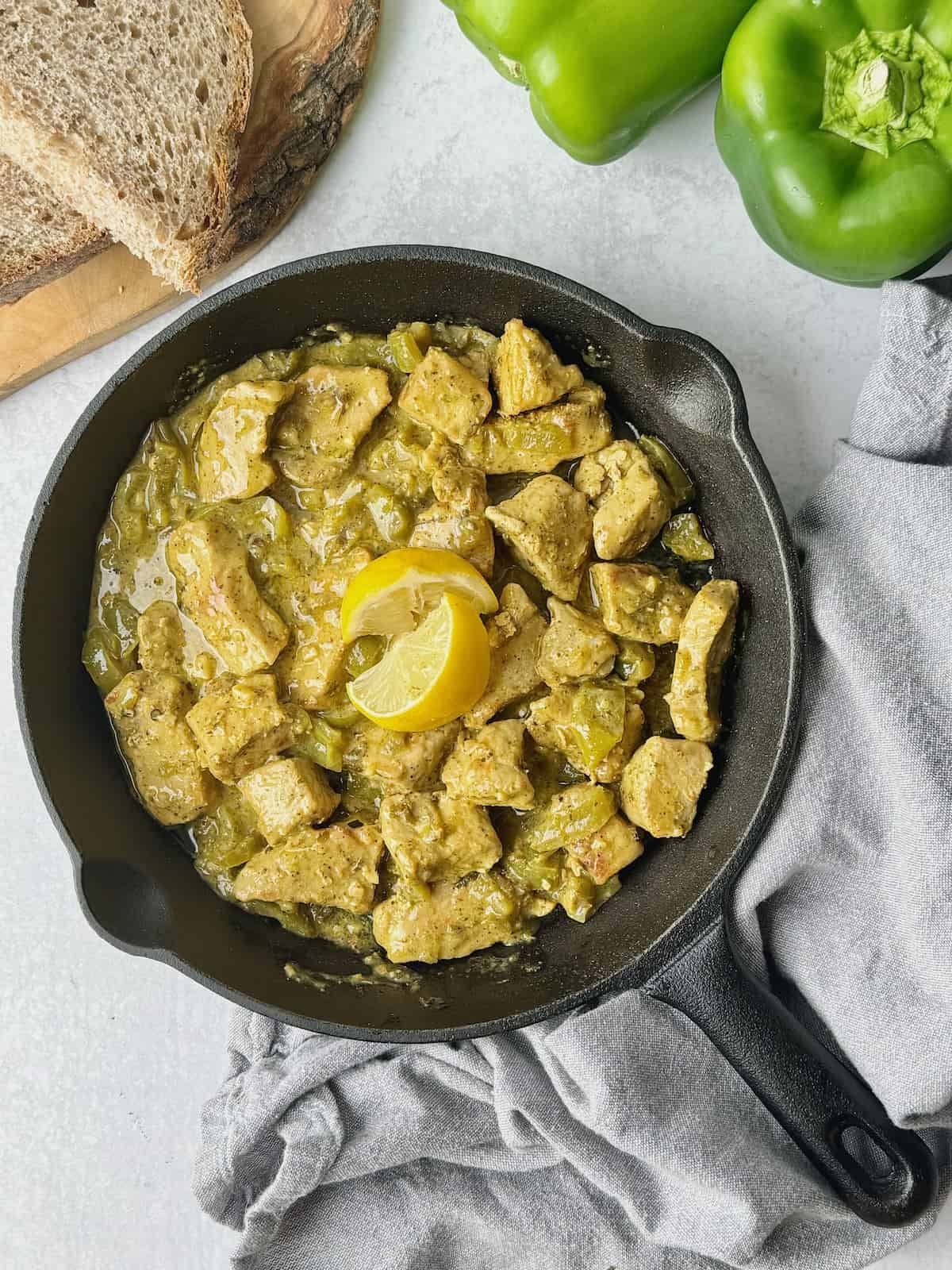 Greek tigania on a frying pan next to peppers and slices of bread.