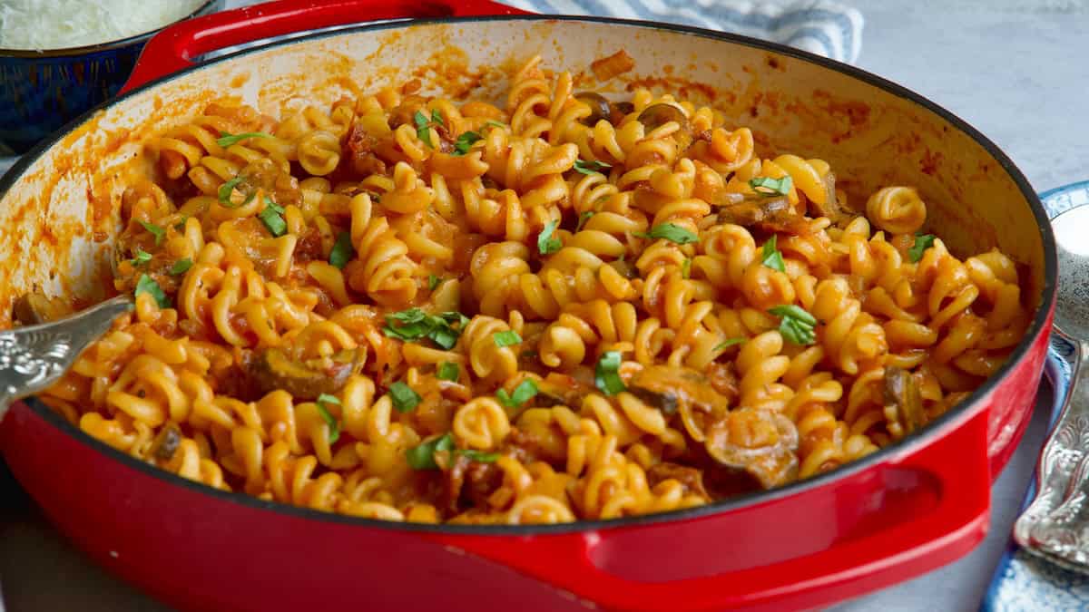 Pasta with mushroom and sun-dried tomatoes in a red cast iron pan.