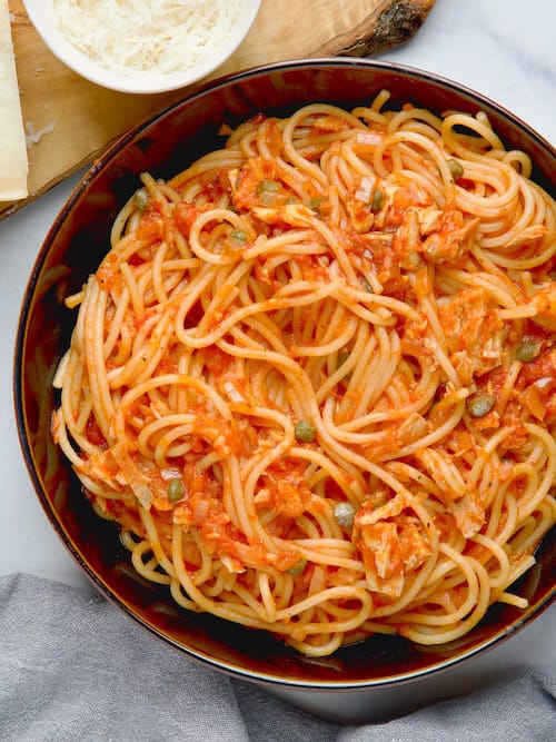 Served pasta with tuna in capers in black bowl with grated parmesan and bowl with capers next to it. Served pasta with tuna in capers in black bowl with grated parmesan and bowl with capers next to it.