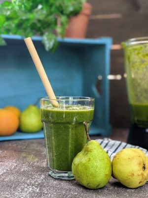 Smoothie αχλάδι και μαρούλι σερβιρισμένο σε ποτήρι με καλαμάκι από μπαμπού δίπλα σε δύο αχλάδια.