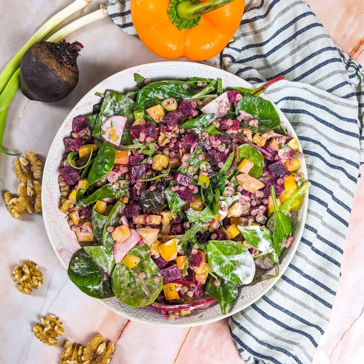 Pearl couscous and beetroot salad served in white bowl next to beetroot, green onions and yellow pepper.