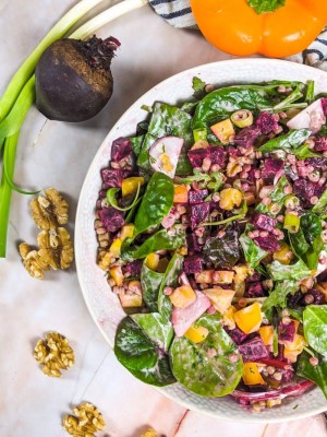 Pearl couscous and beetroot salad served in white bowl next to beetroot, green onions and yellow pepper.