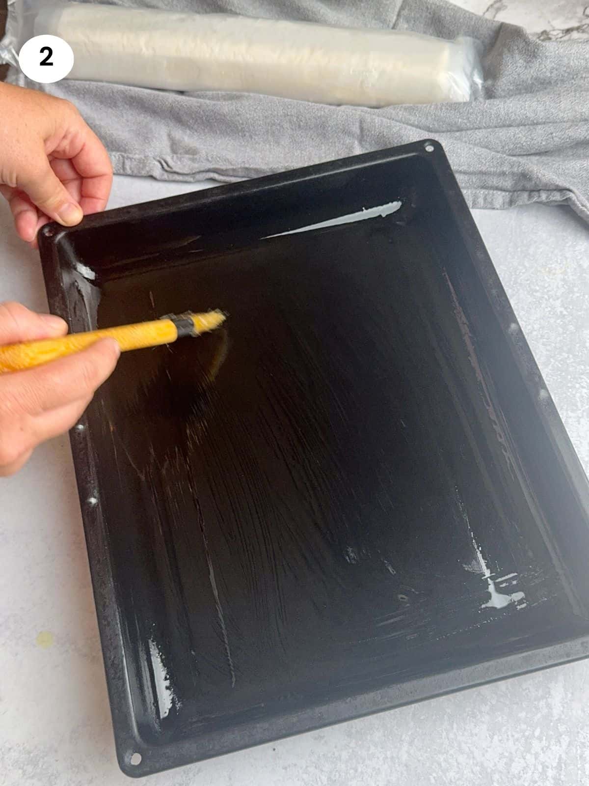 Brushing the tray with the mixture of oil and butter.