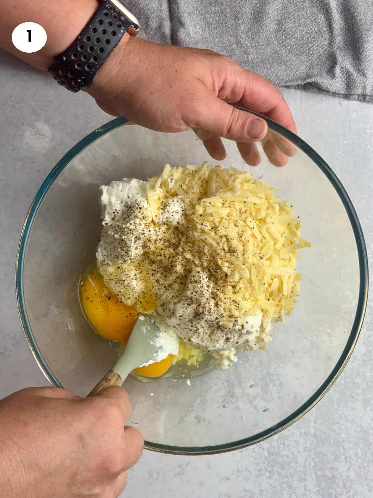 Mixing the different cheeses and eggs in a glass bowl.