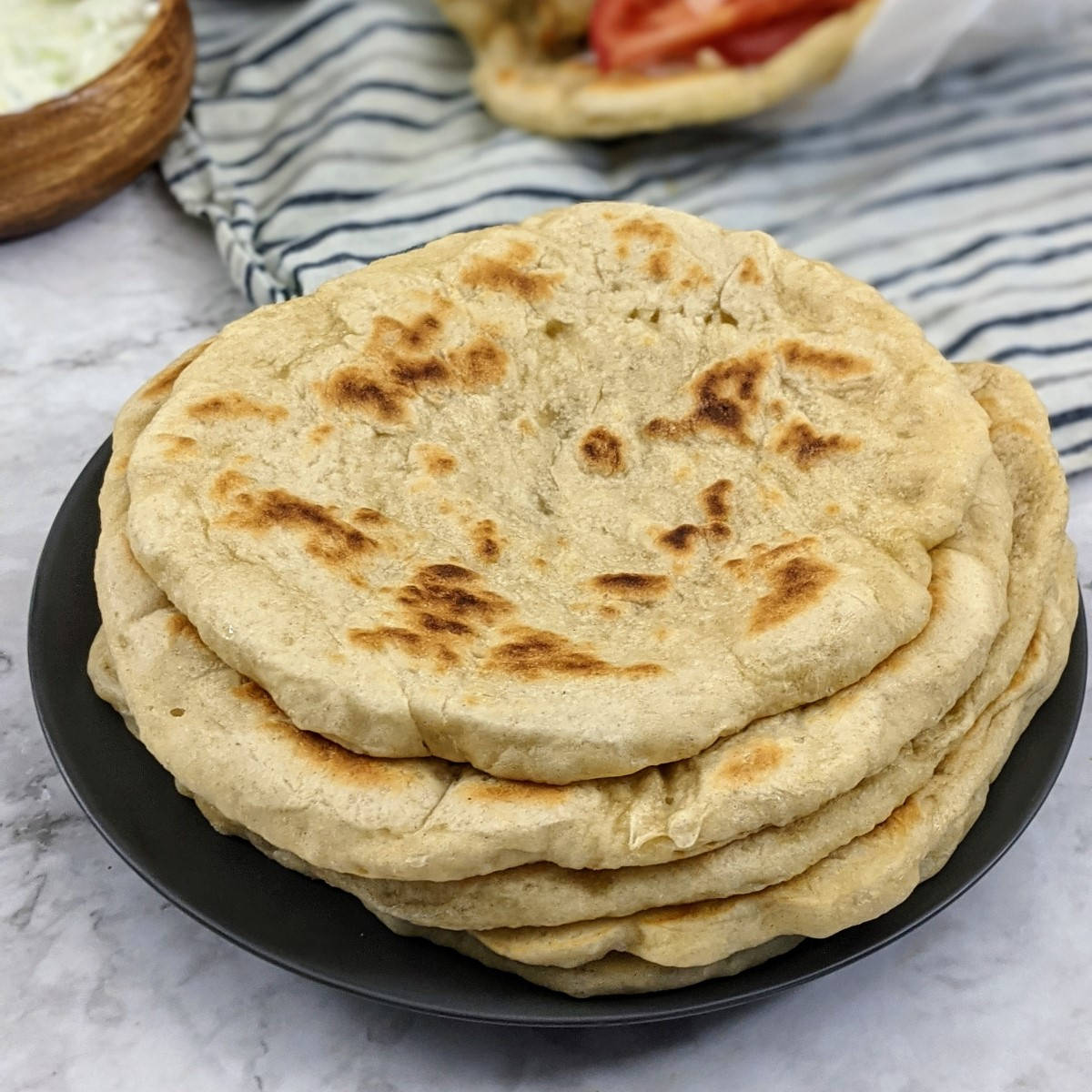 Pita breads stack on top of each other on grey plate and a souvlaki wrap at the back.