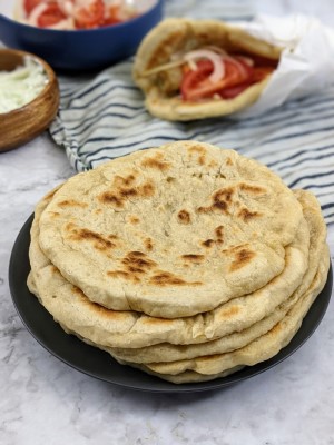 Pita breads stack on top of each other on grey plate and a souvlaki wrap at the back.