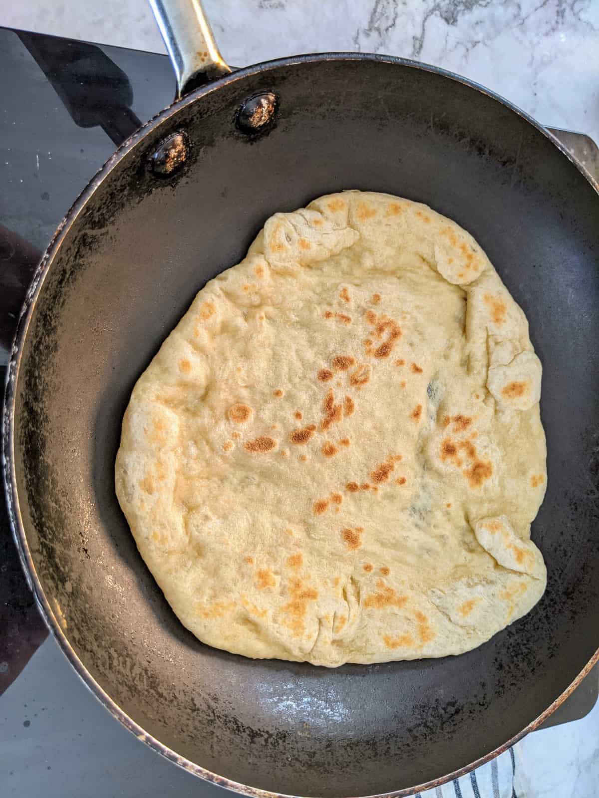 Pita bread on pan with one side already cooked