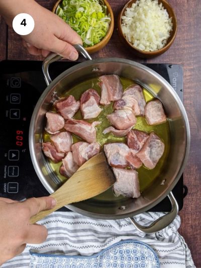 Adding the pork chunks to the pot.