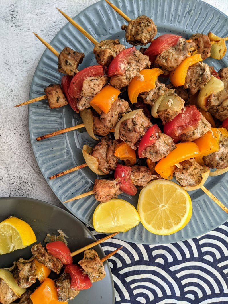 Pork skewers with vegetables stacked on blue plate with two slices of lemon next to them