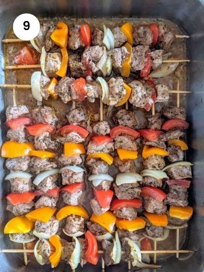 Skewers in the baking tray with water and marinade sauce ready for the oven.