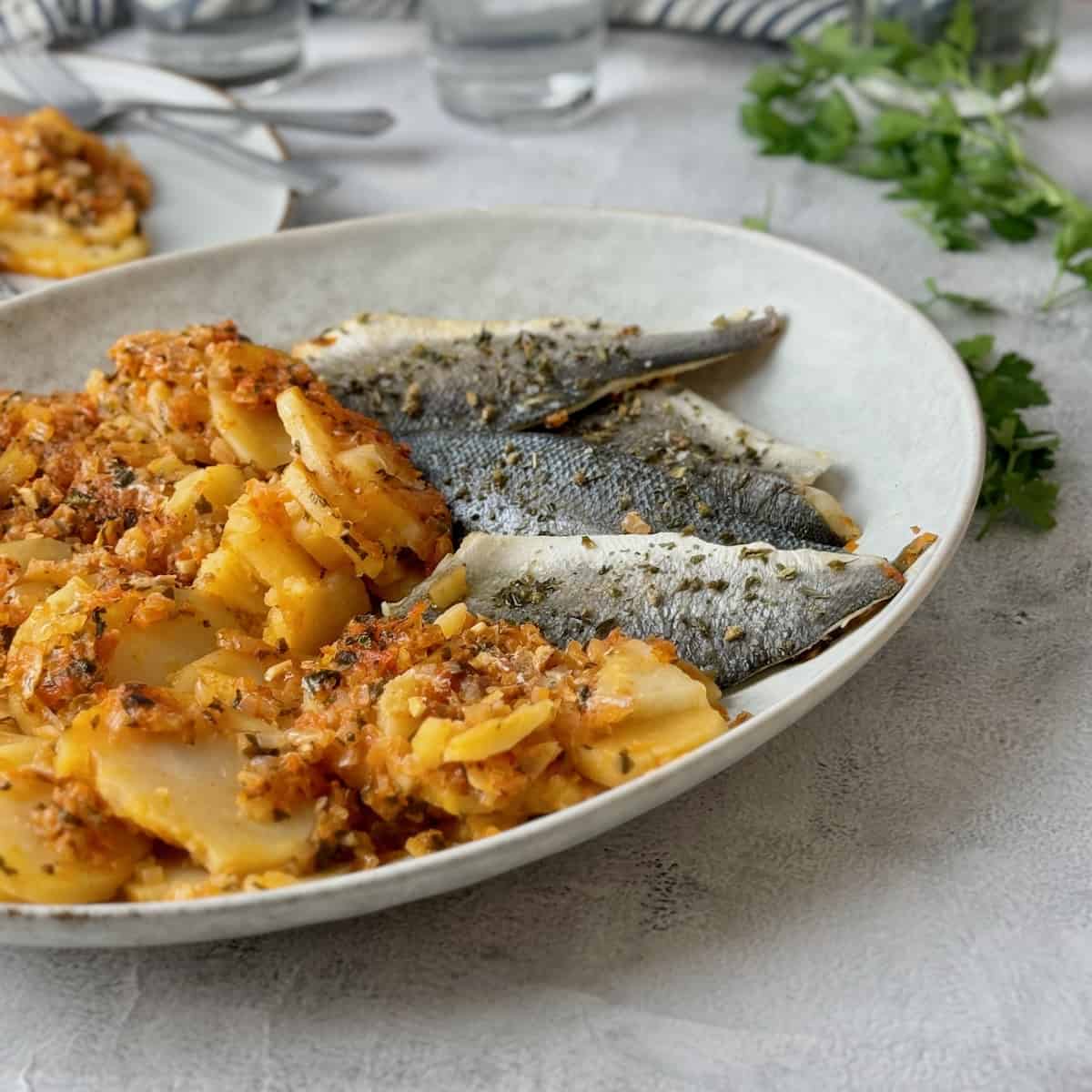 Fish plaki with potatoes served in white serving plate.