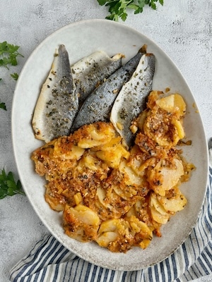 Fish plaki with potatoes served in white serving plate.