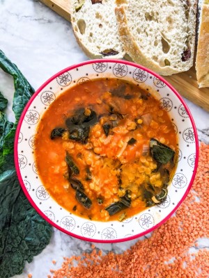 Red lentils and kale soup served in bowl next to slices of olive bread.