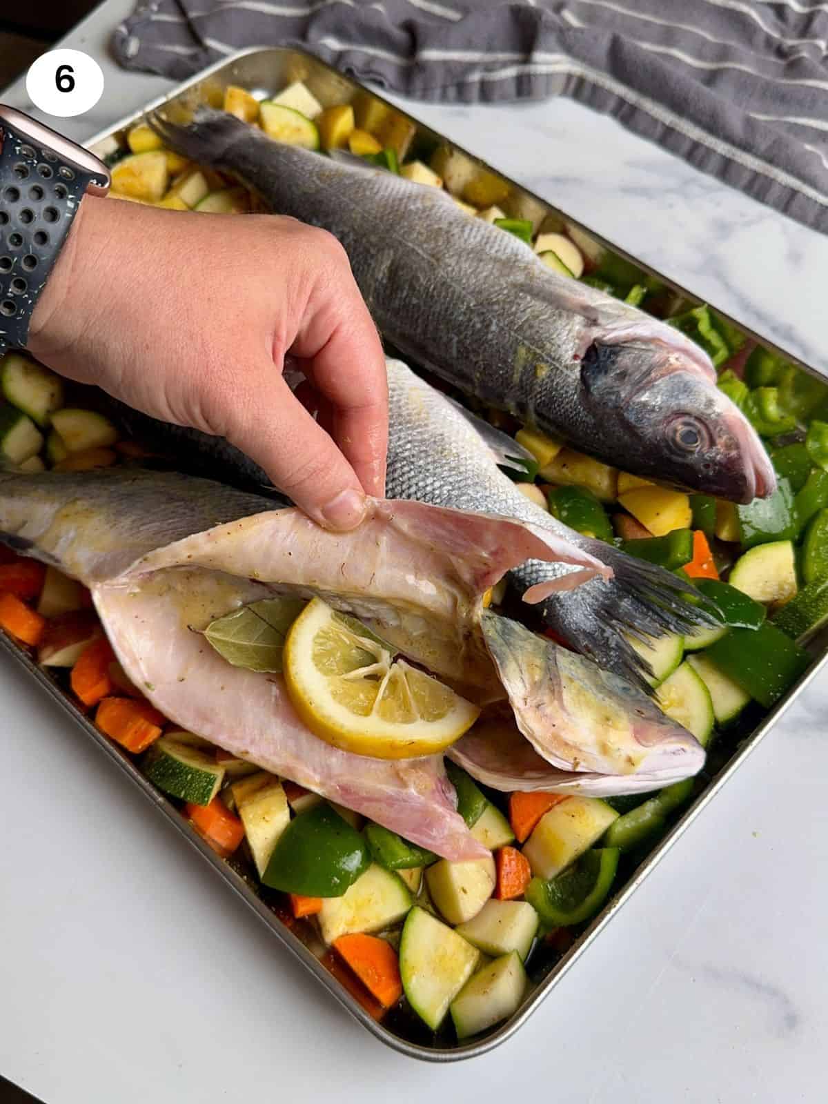 Adding a lemon slice and bay leaf inside the fish.