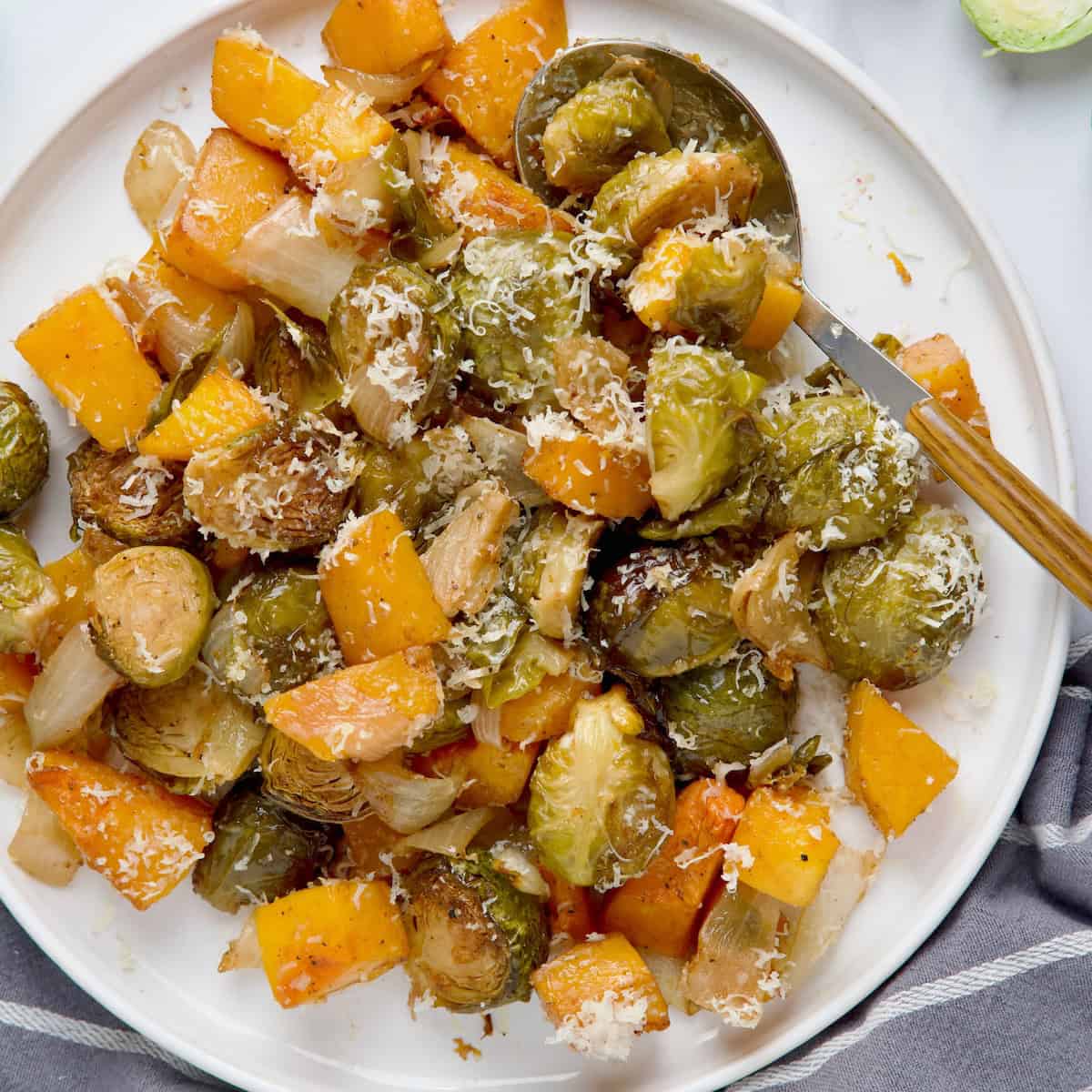 Roasted Brussels sprouts with butternut squash served on white plate next to raw Brussels sprouts.