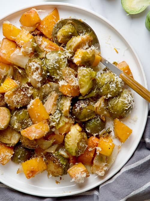 Roasted Brussels sprouts with butternut squash served on white plate next to raw Brussels sprouts.