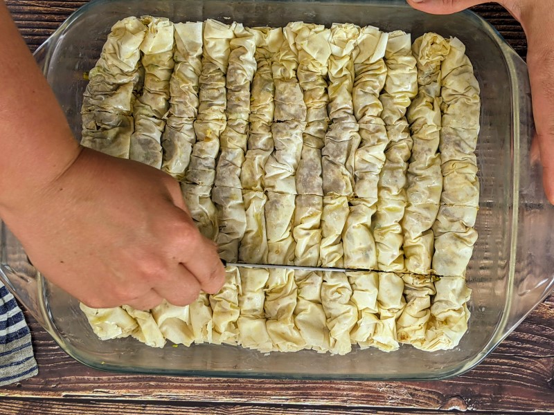 Cutting long baklava rolls into smaller bites before putting it in the oven.