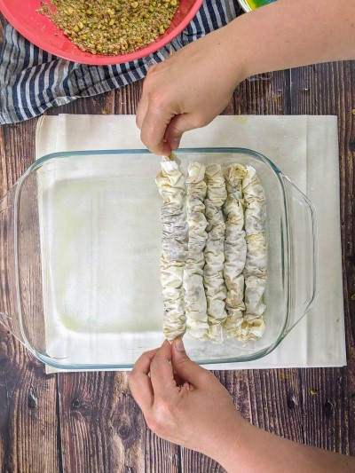 Removing wooden sticks whilst placing baklava roll in tray.