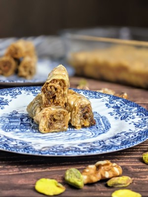 Rolled baklava bites served on a plate next to some walnuts and pistachios