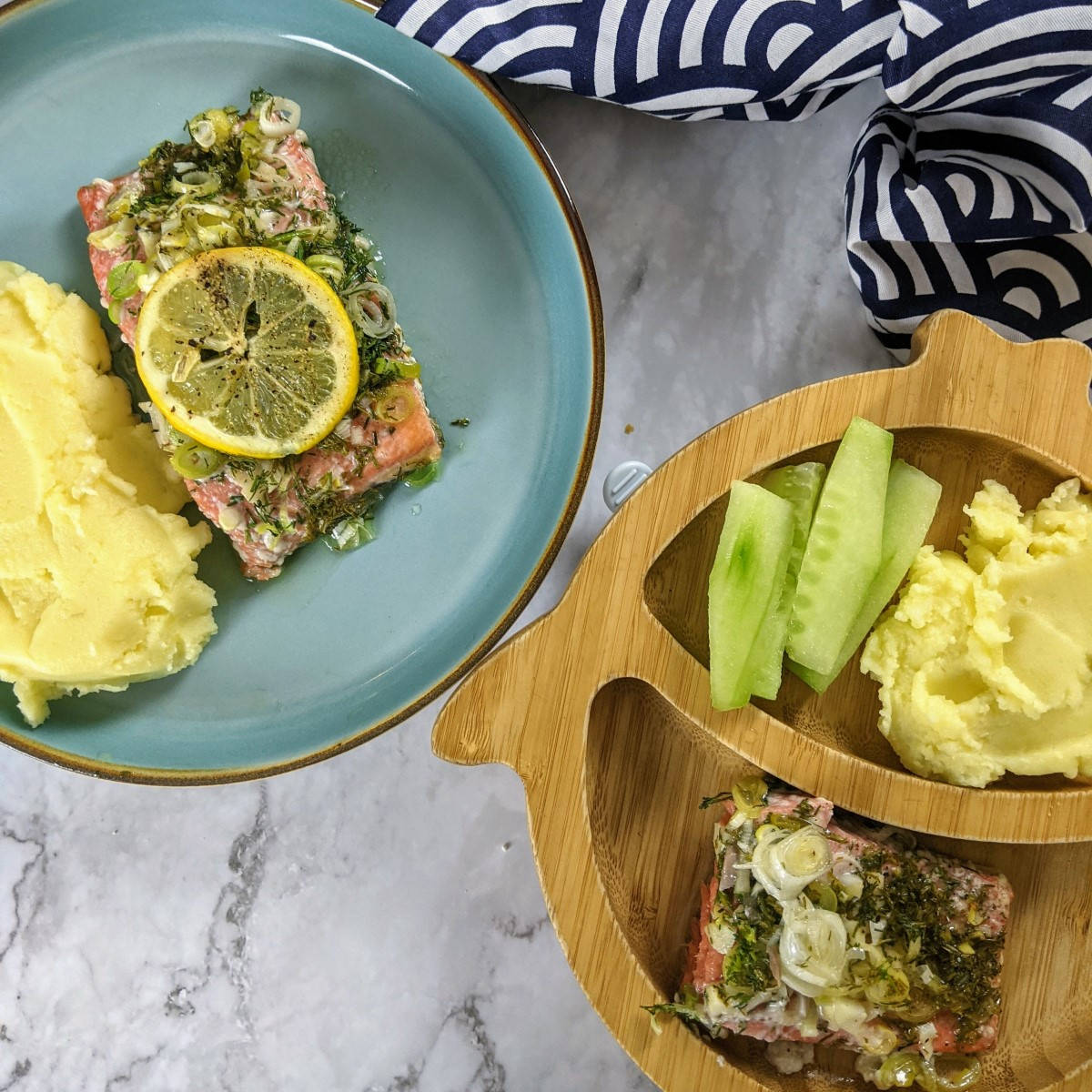 Salmon fillet served with lemon on top and mash on the side in an adult and a toddler bamboo plate