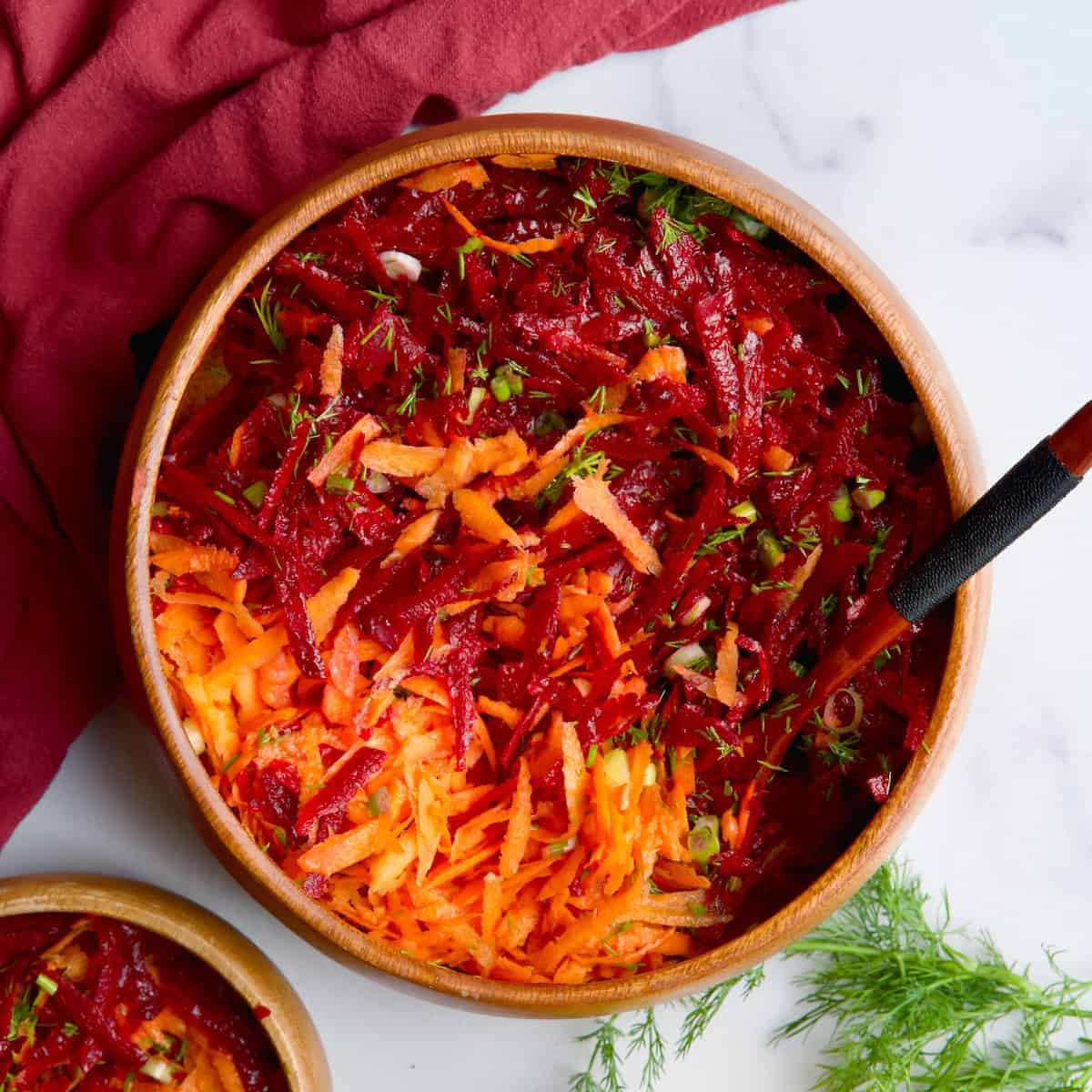 Beet and carrot salad in wooden bowl next to lemon slices, olive oil and fresh dill.