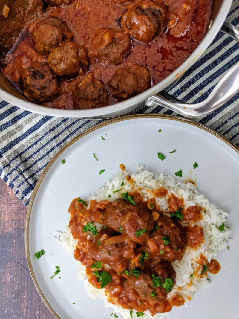 Meatballs with tomato sauce served on top of rice and sprinkled with chopped parsley