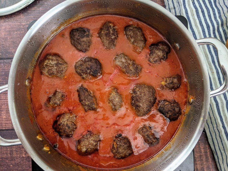 Placing soutzoukakia meatballs on top of the tomato sauce.