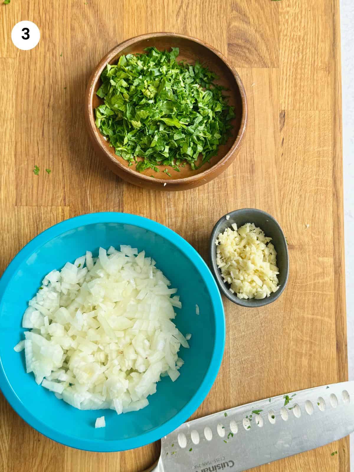 Chopped onion, garlic cloves and fresh parsley in bowls.