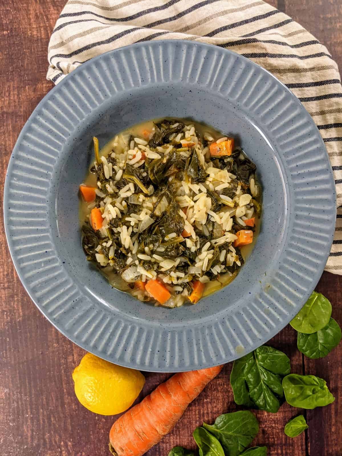 Spinach and rice stew served on a blue plate on top of tea towel with stripes