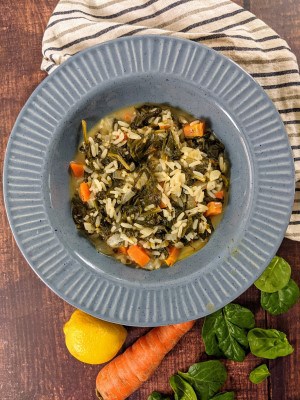 Spinach stew with rice served in a blue plate next to carrots, spinach and a lemon.