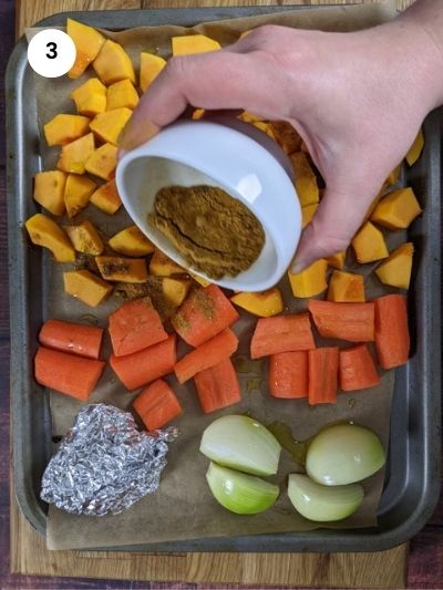 Adding the mix of spices to the veggies on the sheet pan.