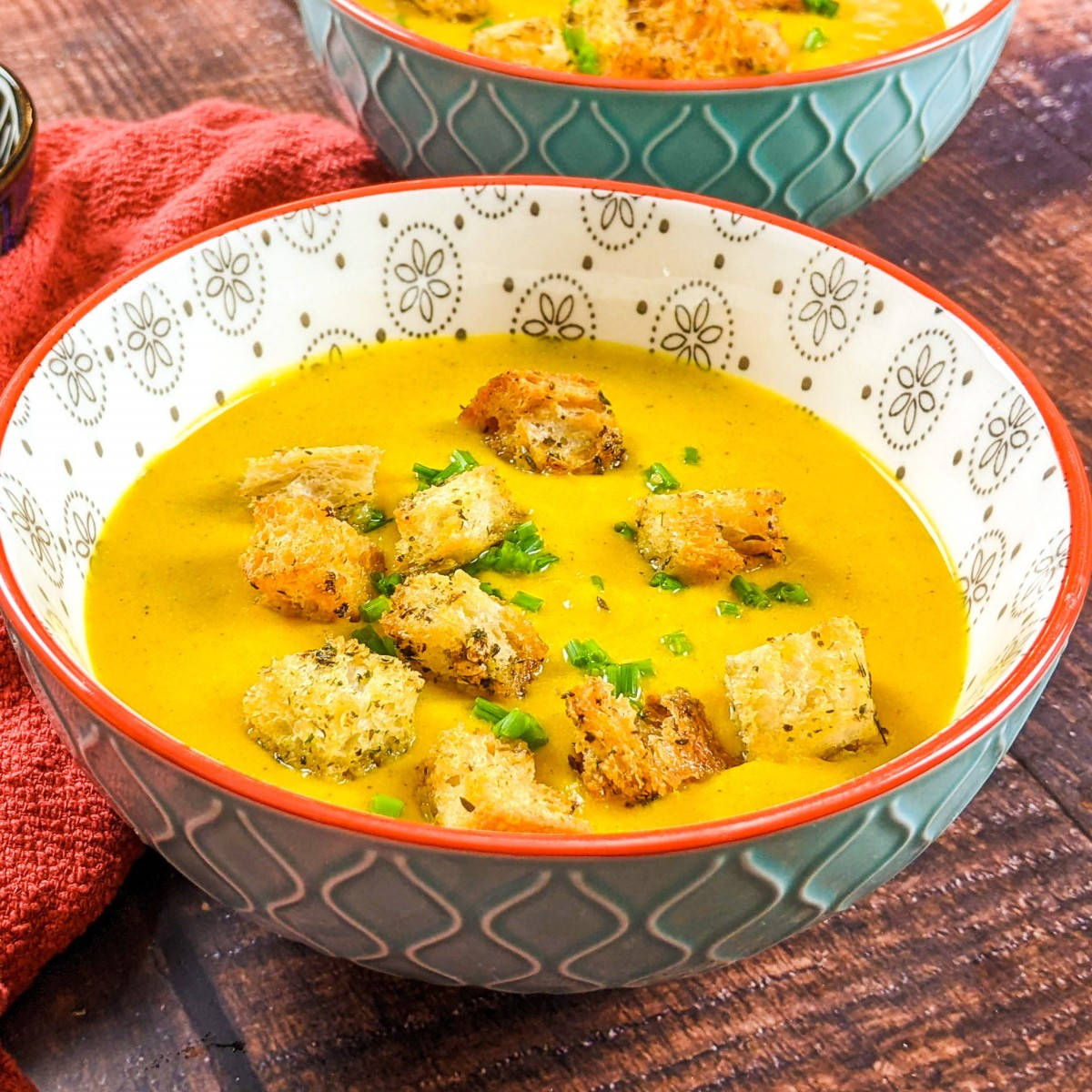 Butternut squash soup served in a blue bowl and garnished with chives and croutons.