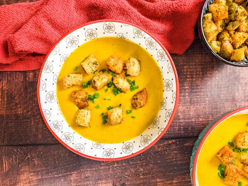 Butternut squash soup served in a blue bowl and garnished with chives and croutons.