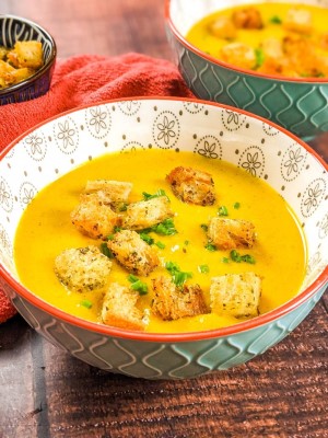 Butternut squash soup served in a blue bowl and garnished with chives and croutons.