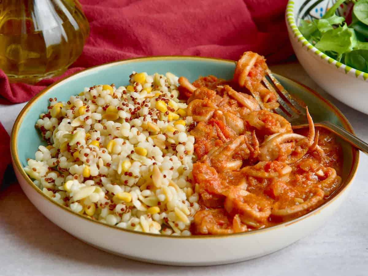 Squid in tomato sauce served with mixed grains and salad on the back.