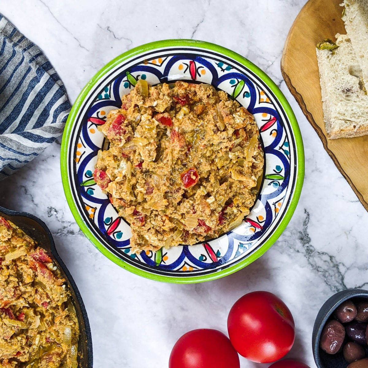 Greek eggs and tomato dish next to bread, olives and tomatoes.
