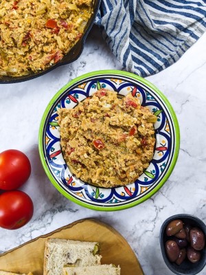 Greek eggs and tomato dish next to bread, olives and tomatoes.