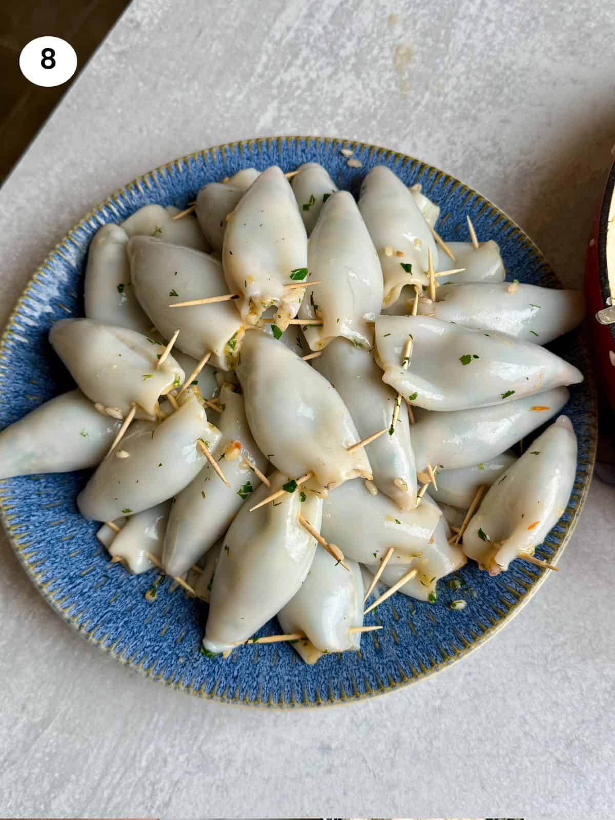 Stuffed calamari with toothpicks on a plate ready to be cooked.