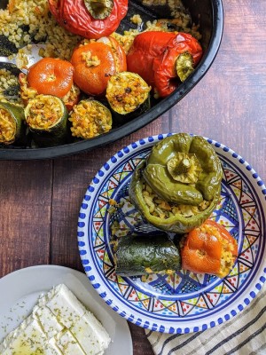 Stuffed pepper, tomato and zucchini served in rustic plate next to a slice of feta cheese and oven tray