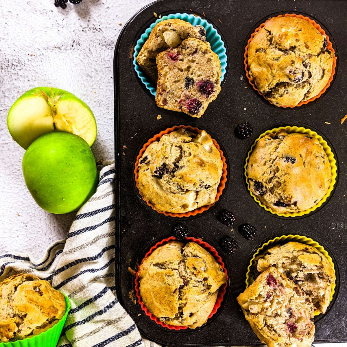 Sugar free blackberry muffins in a baking tray next to blackberries and a green apple.