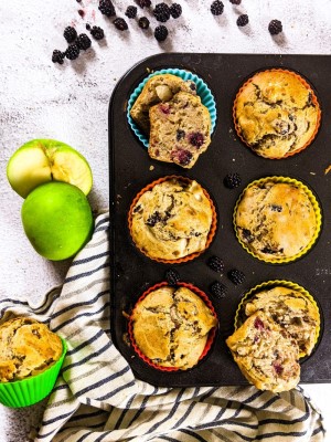 Sugar free blackberry muffins in a baking tray next to blackberries and a green apple.